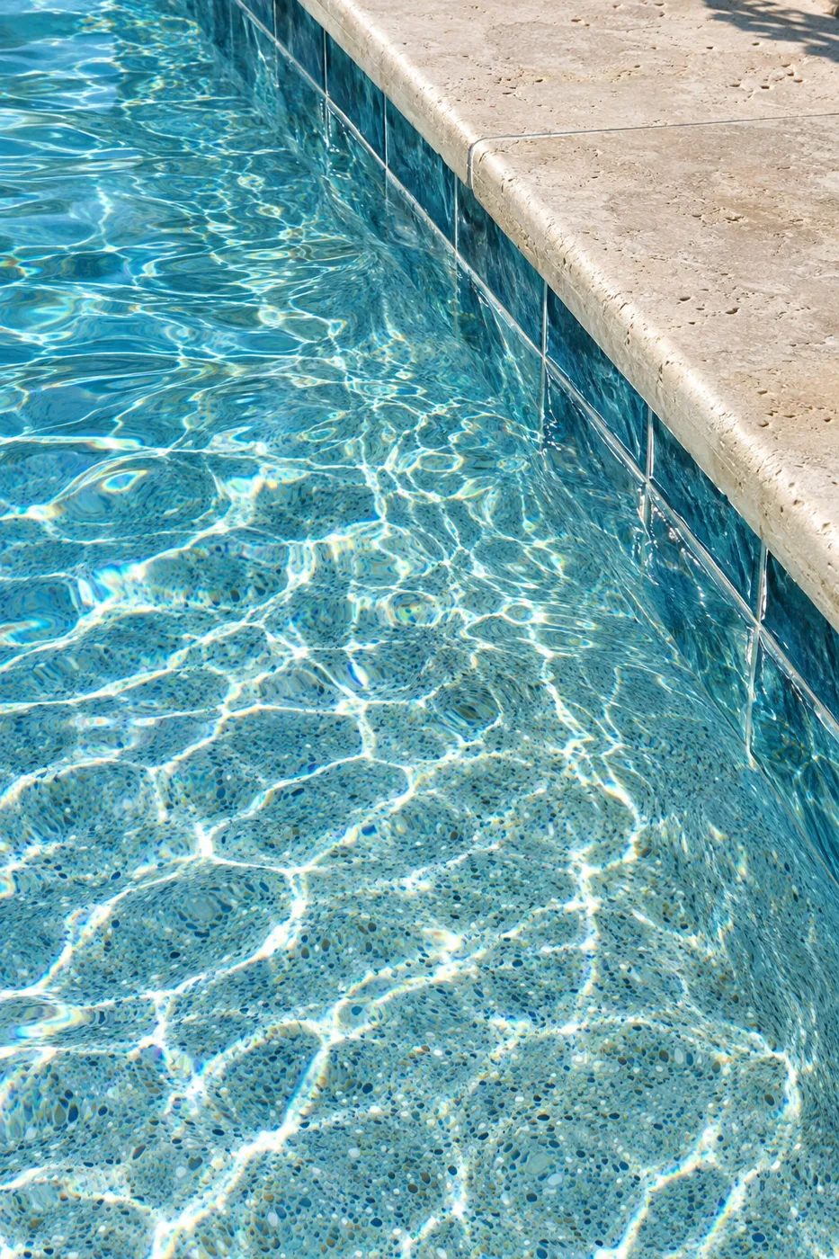 Close-up of clear water over a blue pebble pool finish and travertine coping